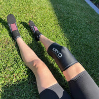 Woman wearing a KRYO CORE cold compression sleeve on her knee while recovering outdoors after exercise.