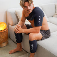 Male athlete seated on a couch wearing the KRYO Shoulder Sleeve for targeted shoulder and upper arm compression, alongside two KRYO CORE hot and cold compression sleeves on his lower legs.
