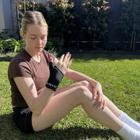 Woman wearing the KRYO Wrist Compression Ice Sleeve outdoors, featuring a flexible hot and cold gel design for targeted wrist and forearm recovery.
