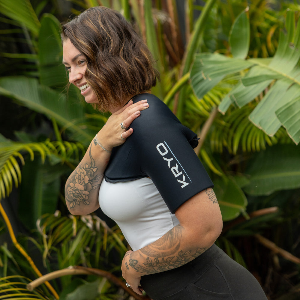 Woman smiling outdoors while wearing the KRYO Shoulder Ice Compression Sleeve, providing targeted cold and heat therapy for the shoulder, bicep and upper arm.